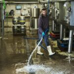 Man working in a brewery, cleaning floor with water hose.