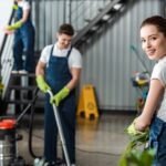 attractive cleaner smiling at camera while colleagues cleaning office