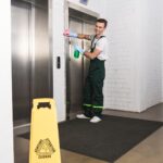 handsome young janitor cleaning elevator and smiling at camera